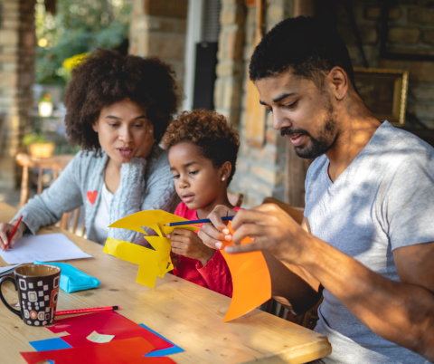 The image shows a family sitting at a table working on a craft project together.